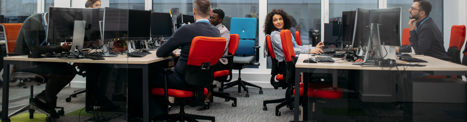 An image of people in an office space with red task chairs and desks