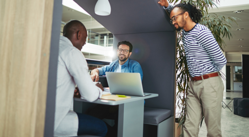 An image of three males working in an office meeting pod with a laptop.