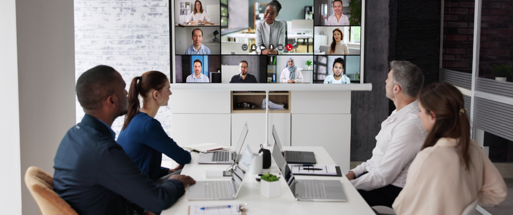 Staff around a meeting table with people in a video call on a monitor