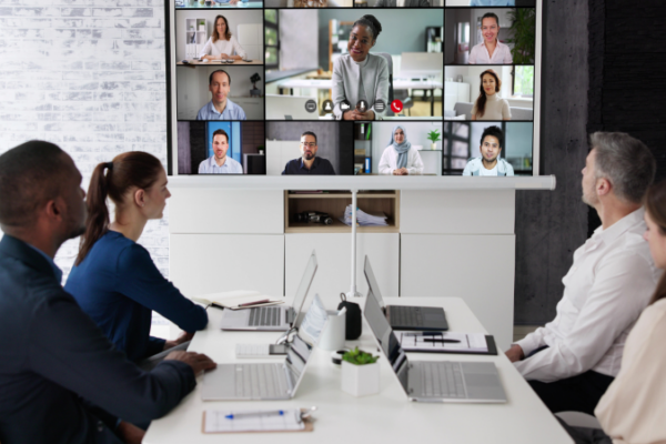 Staff around a meeting table with people in a video call on a monitor