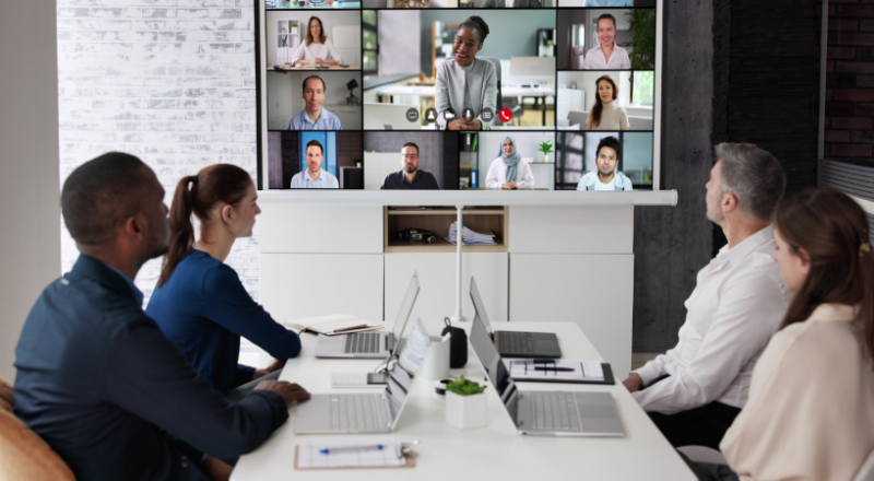 Staff around a meeting table with people in a video call on a monitor