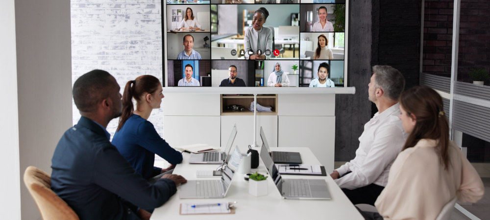 Staff around a meeting table with people in a video call on a monitor